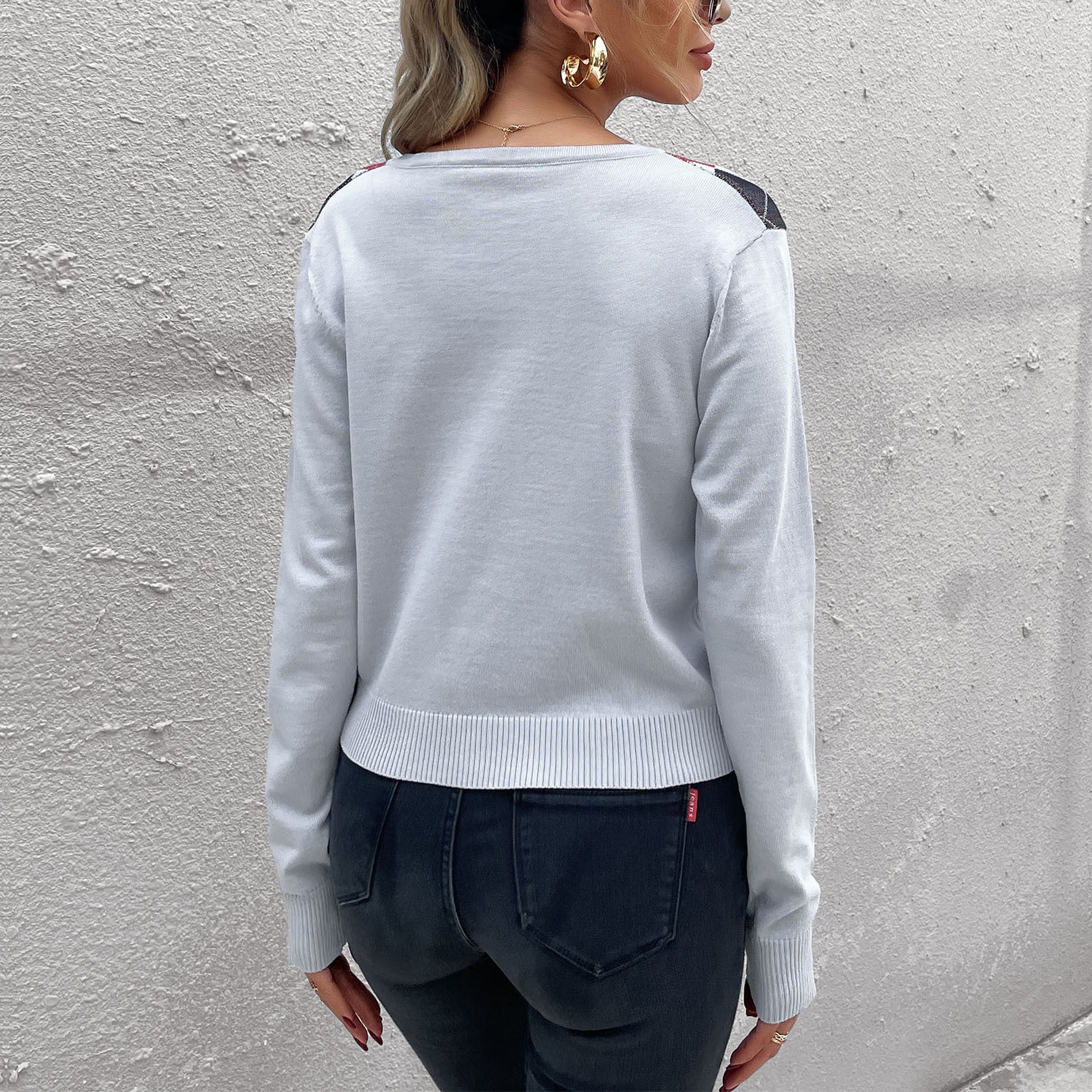 A woman showing back view of light gray cardigan sweater with ribbed hem, paired with dark jeans against white background