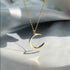 Gold crescent moon necklace with shadow casting on white fabric, showing minimalist design
