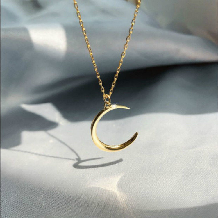 Gold crescent moon necklace with shadow casting on white fabric, showing minimalist design