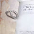 A silver twig-shaped open band ring resting on a book page, with visible text and 'Flirtin' visible in the background