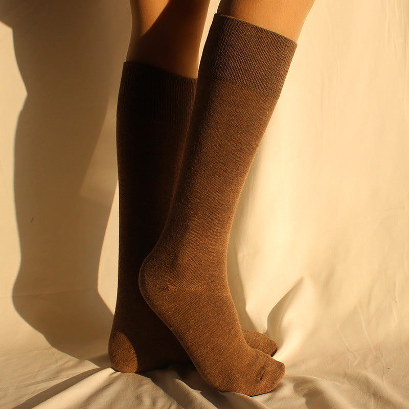 Person wearing knee-high brown cotton socks against cream background with warm lighting and shadow effect