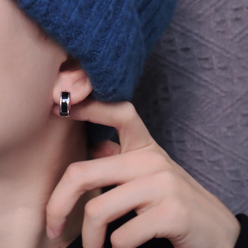 Silver and black huggie hoop earring worn on ear with blue knit garment