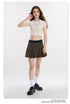 Model with long brown hair in white crop top, plaid mini skirt, white socks and black platform shoes against white background