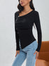 Close-up of black ruched top with diagonal white button detail and V-neckline, styled with denim