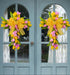  Matching yellow and pink floral cross wreaths with bows, symmetrically displayed on blue double doors for a festive look.