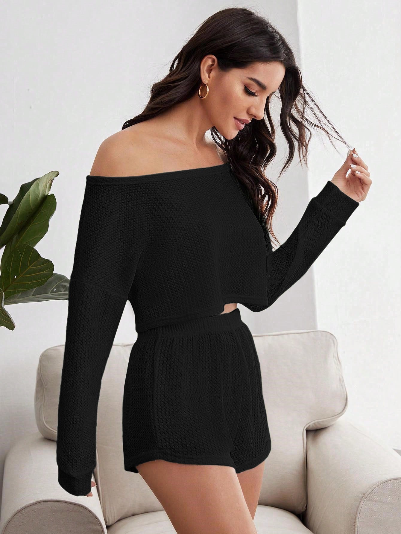 Side profile of woman in black loungewear set with textured fabric, posing on beige couch