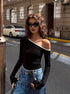 Black one-shoulder top with white trim, wavy hair, cat-eye sunglasses, parked cars in urban street setting.