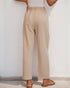 Back view of a woman in beige pleated trousers featuring an elastic waistband, paired with tan sandals.
