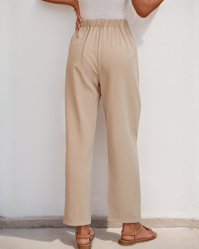 Back view of a woman in beige pleated trousers featuring an elastic waistband, paired with tan sandals.