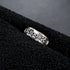 A silver skull ring with crossbones details resting on a black textured surface, emphasizing its rugged and gothic aesthetic.