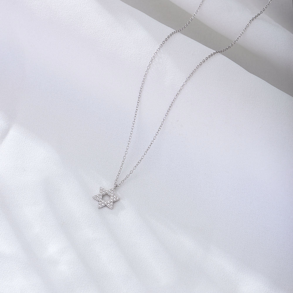 A silver Star of David pendant necklace with crystal accents displayed on white fabric. The minimalist six-pointed star pendant hangs on a fine chain