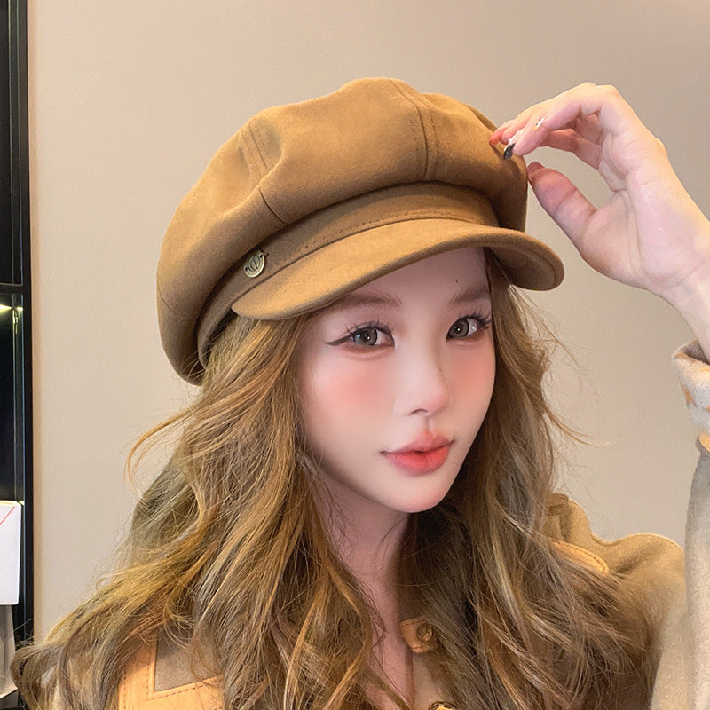Close-up of woman adjusting tan newsboy cap with metal detail, showing wavy brown hair and natural makeup