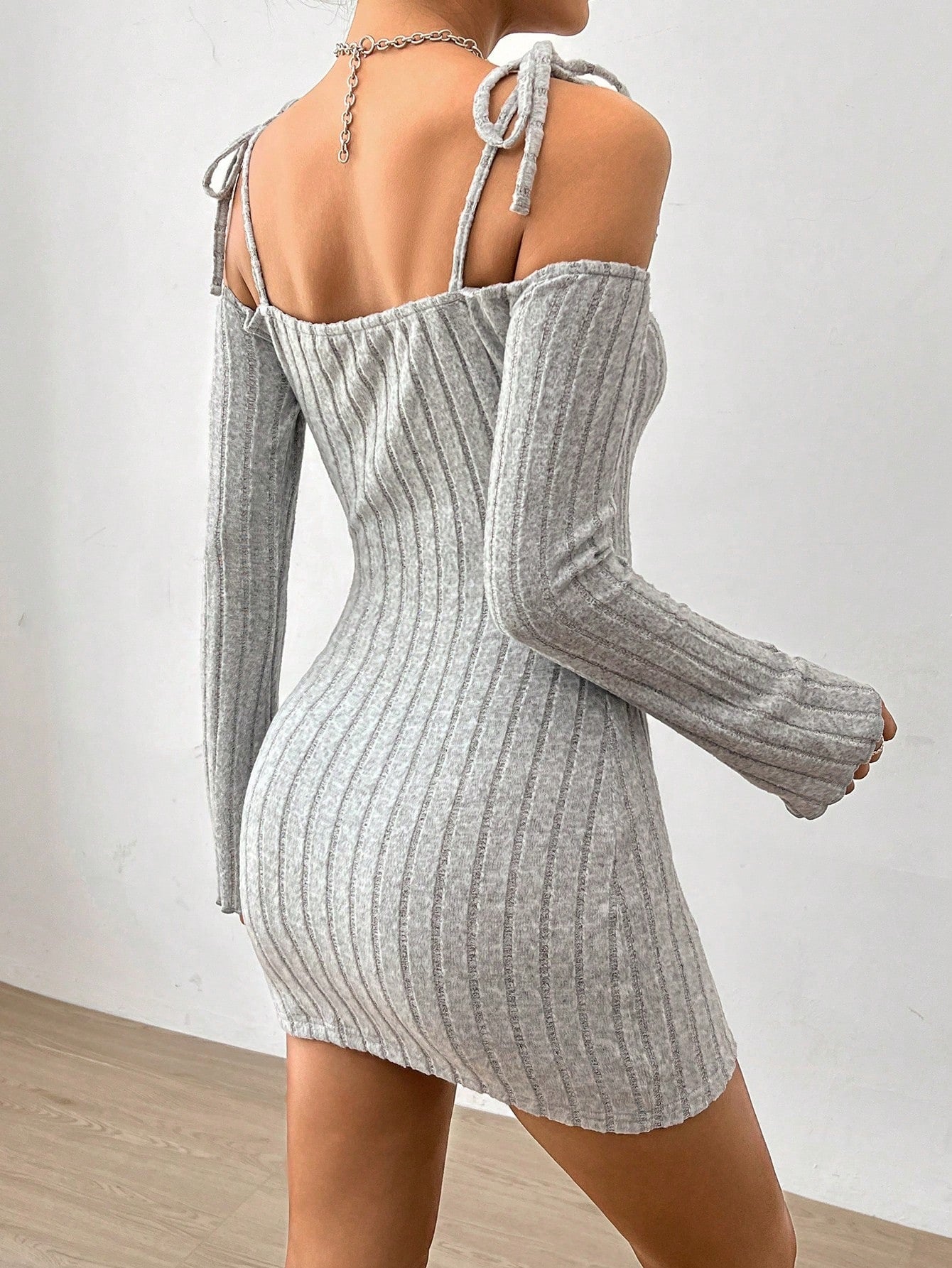 Back view of a woman wearing a gray ribbed mini dress with tie straps and long sleeves, highlighting its fitted silhouette