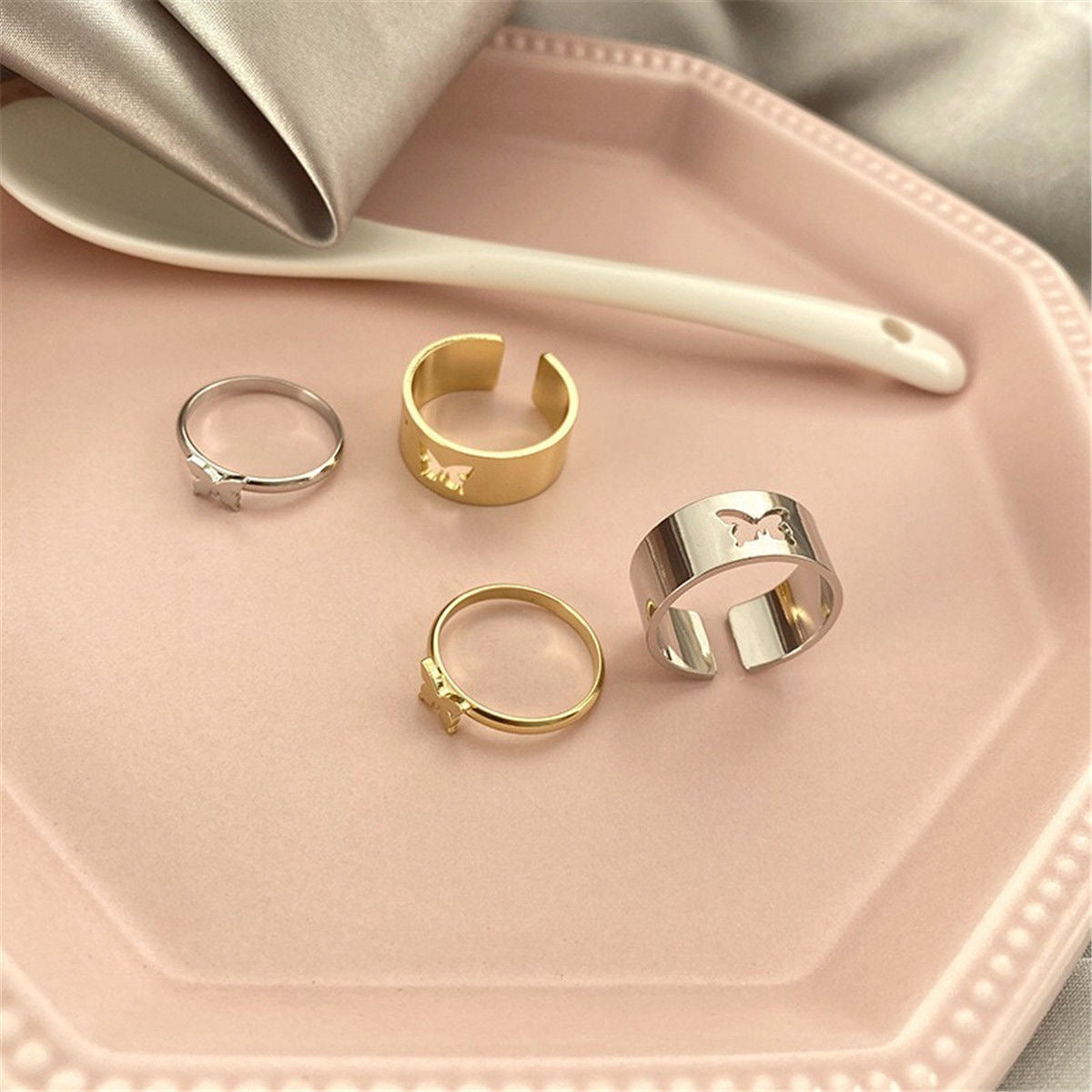 Butterfly ring set arranged on pink plate: two wide bands and two thin bands in mixed metals