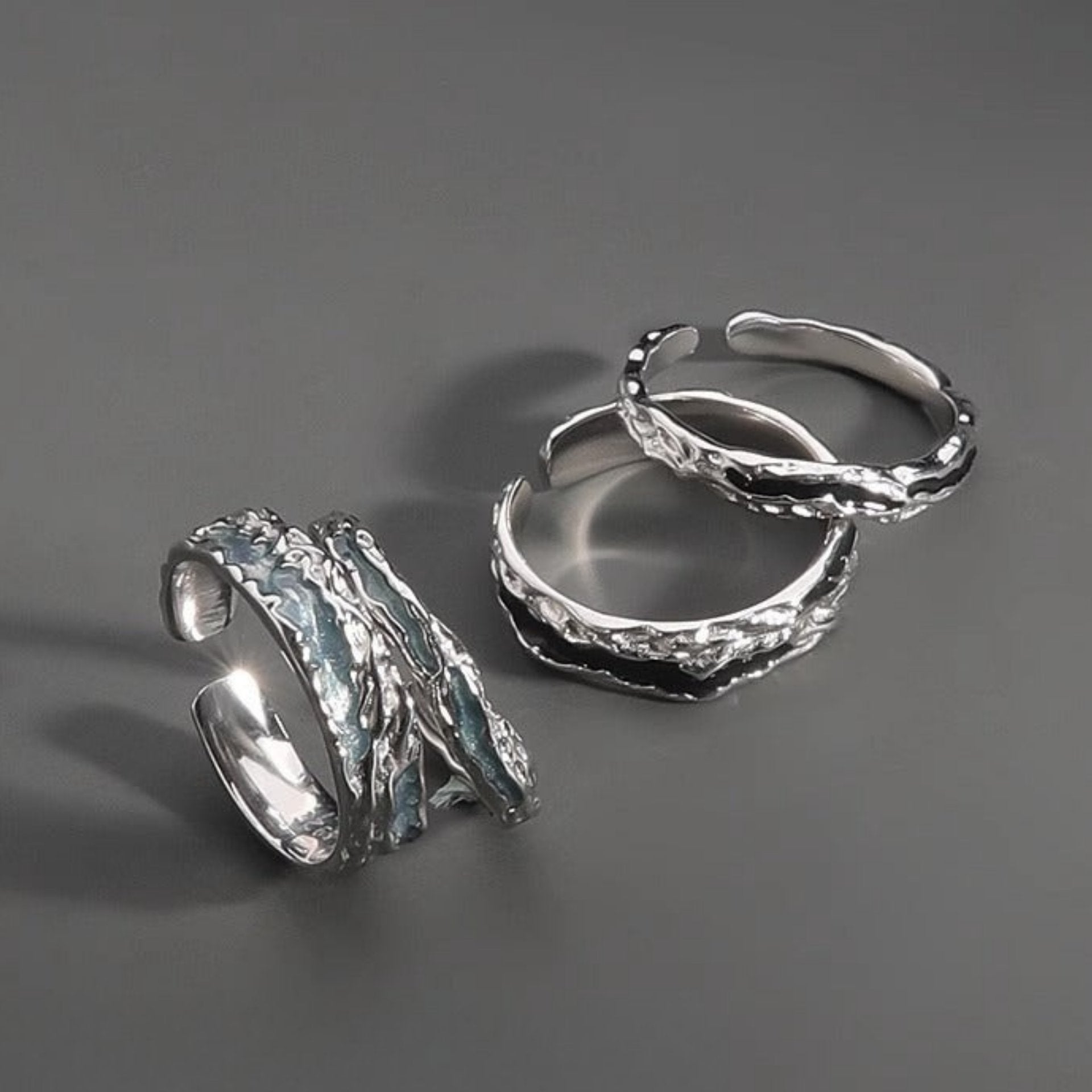 Four textured silver rings displayed on a gray surface