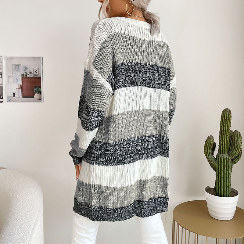 A back view of woman in white and gray striped cardigan with white pants, showing oversized silhouette against wall with cactus plant on side table