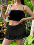 Woman in black crop top and ruffle skirt holding silver phone case, styled with mini bag in garden setting