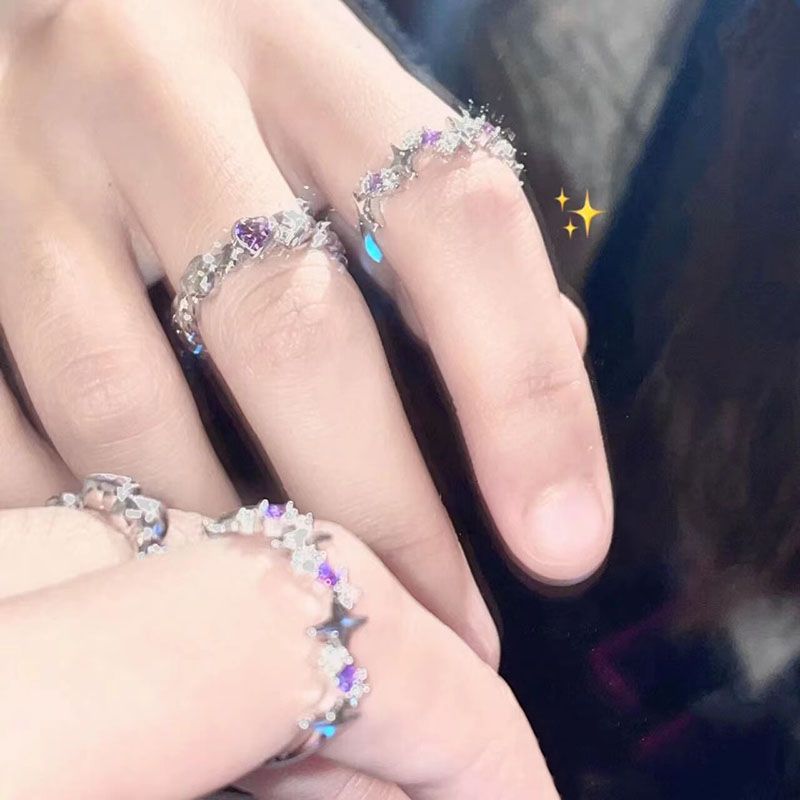 A person wearing multiple silver rings with purple crystal accents and star designs on their fingers against dark background with star emoji