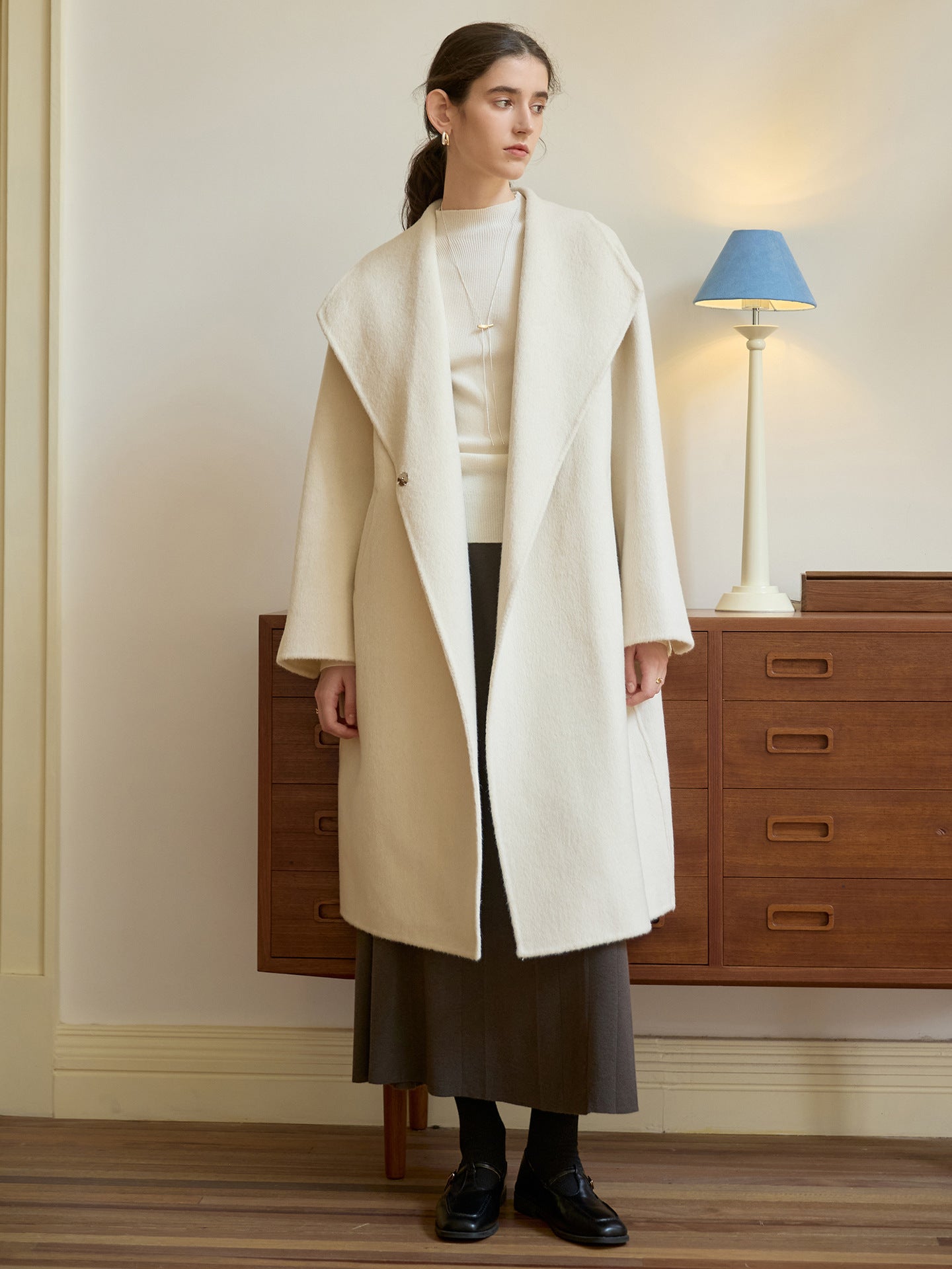 Full-length view of cream wool coat styled with ribbed sweater and dark midi skirt