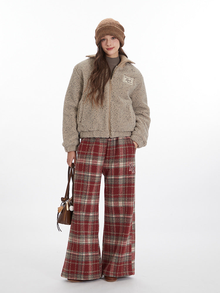 Model in full-length pose wearing beige sherpa jacket, brown beanie, plaid pants and carrying small brown bag against white backdrop