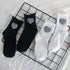 Four crew socks with gingham heart patches arranged in pairs of black and white on a grid background