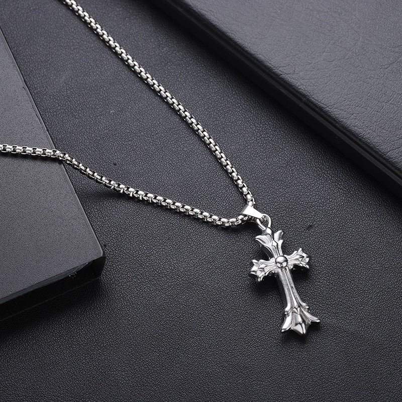 Box chain necklace with decorative cross pendant on dark leather surface