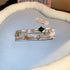 Wavy silver alligator hair clip with pearl and multicolored gemstone accents, displayed on soft fabric.