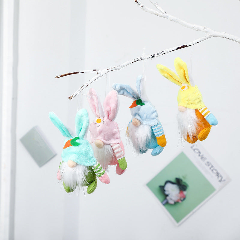 Four hanging plush bunny gnome ornaments in pastel colors, suspended from a white tree branch, featuring long ears and soft beards.