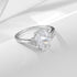 A silver engagement ring with pear-shaped diamond center and triangle accent stones, displayed on white fabric surface with soft shadows