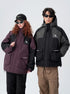 A man and woman wearing contrasting All Drifting jackets stand against white background - his in black/gray, hers in plum/black