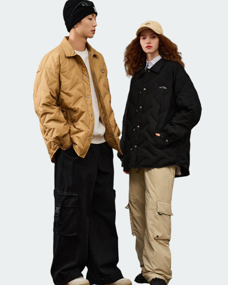 Two models in coordinated winter wear posing casually, man in tan quilted jacket and black beanie, woman in black quilted jacket and beige cap