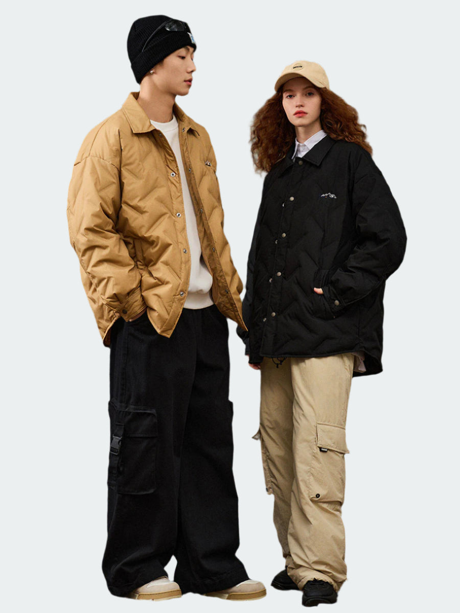 Two models in coordinated winter wear posing casually, man in tan quilted jacket and black beanie, woman in black quilted jacket and beige cap
