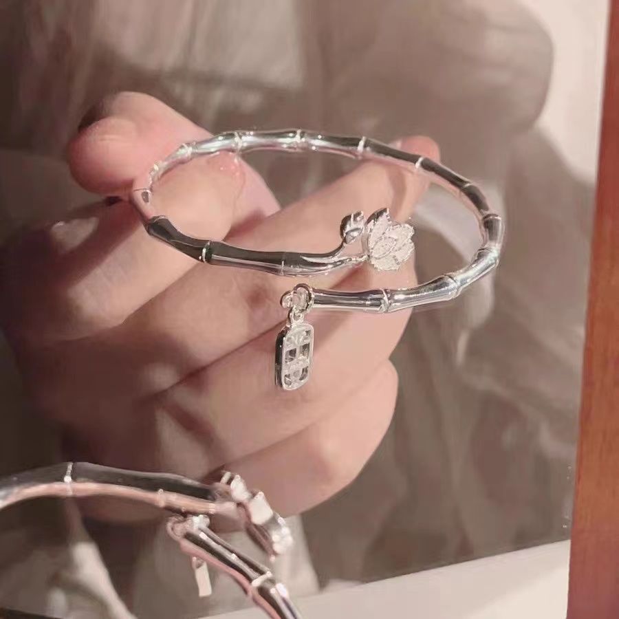 A silver bamboo-inspired bracelet with lotus flower and rectangular charm displayed in hand against light fabric