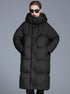 A woman wearing a black quilted oversized puffer coat with wide hood, black sunglasses and red lipstick, posing against gray background