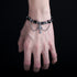  A person's hand adorned with a black and silver beaded bracelet, highlighting the gothic-inspired cross pendant and layered chain design.