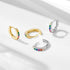 A pair of silver huggie hoop earrings with colorful rainbow gemstones arranged in sequence on minimalist backdrop