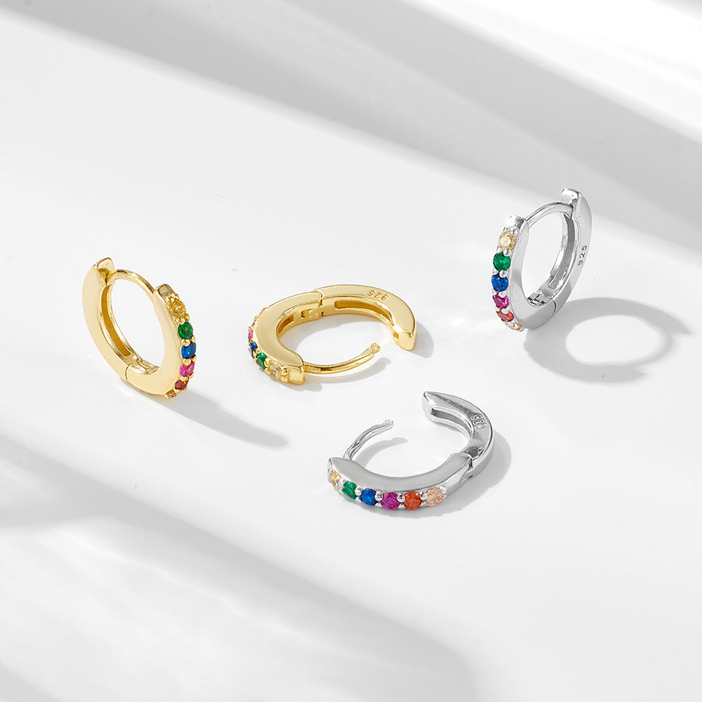 A pair of silver huggie hoop earrings with colorful rainbow gemstones arranged in sequence on minimalist backdrop