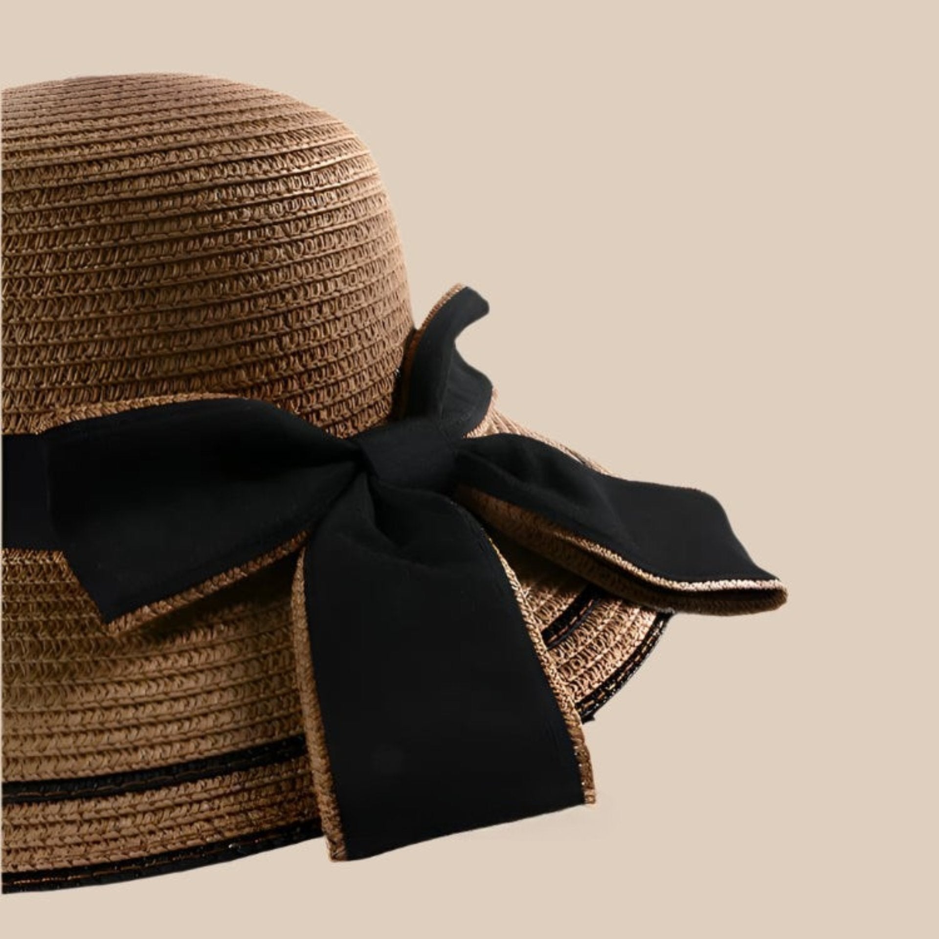 A close-up of a khaki straw sun hat's black bow detail, highlighting the fine texture and craftsmanship.