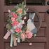 An Easter-themed wreath with a rustic bunny cutout, soft pink flowers, and ribbon accents, hanging on a brown door.