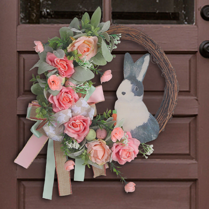 An Easter-themed wreath with a rustic bunny cutout, soft pink flowers, and ribbon accents, hanging on a brown door.