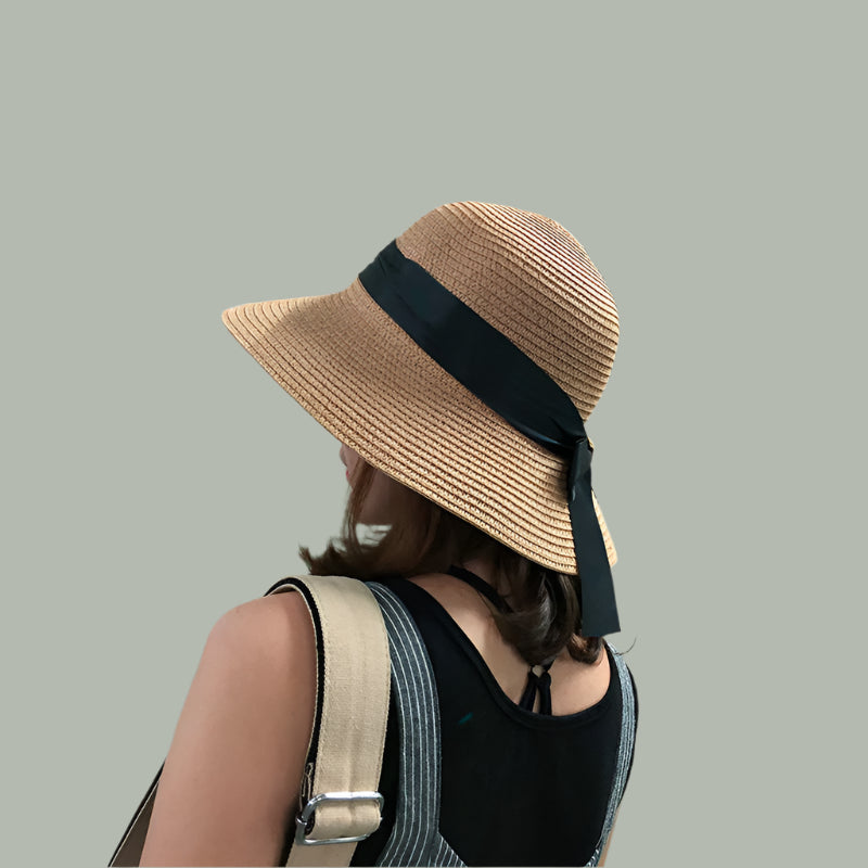 Woman in a straw sun hat with a black ribbon bow carrying a canvas bag.