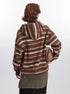 Back view of model wearing textured brown striped hoodie jacket, showing olive green knitted belt detail and carrying matching brown handbag