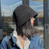 Close-up of a black straw bucket hat with open-weave detailing, styled with a denim jacket and layered necklaces for a chic, casual look.