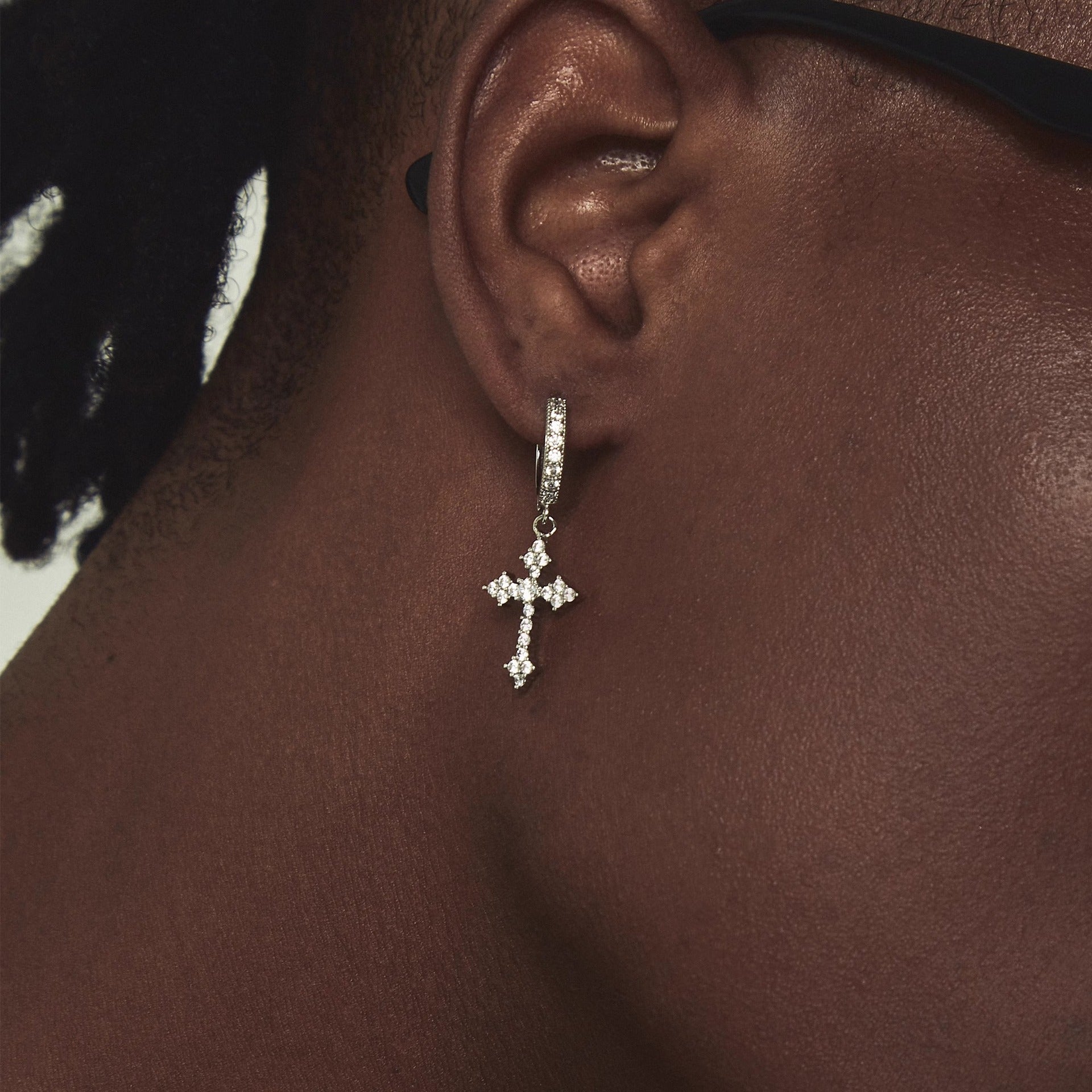Close-up of zircon cross drop earring on dark skin, showing sparkly hoop and dangling cross pendant