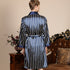 Back view of man in navy striped silk robe with satin trim. Close-up shows belted waist detail and elegant drape against vintage furniture background