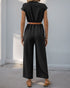 Back view of a woman in a black jumpsuit, showcasing its relaxed fit and cinched waist with a tan belt.