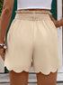 A model showing back view of beige scalloped hem shorts with high paperbag waist and white crop top