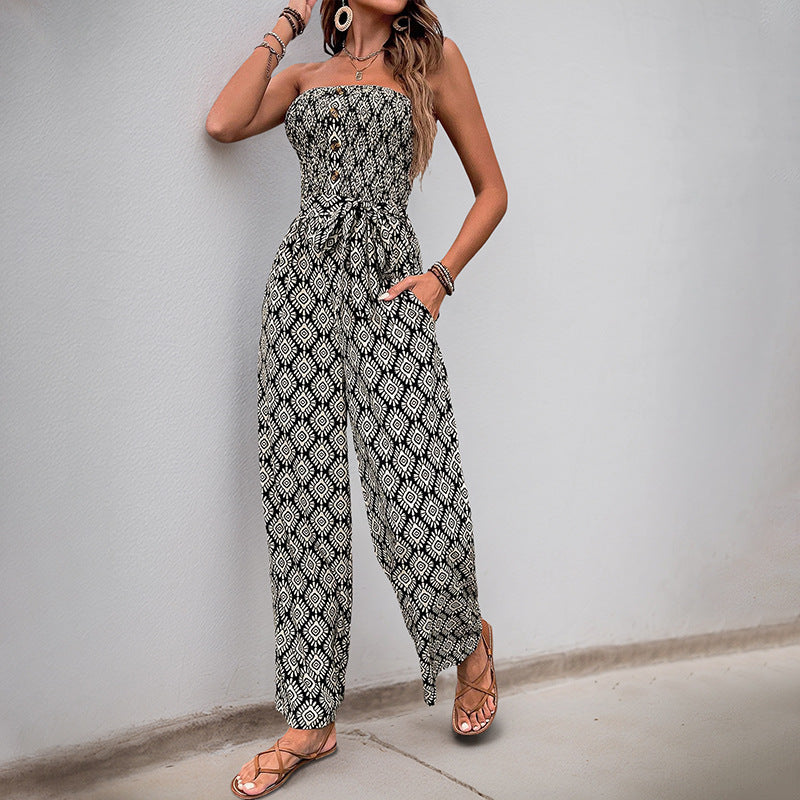 Side view of a woman posing in a black and white strapless jumpsuit with a tie waist, accessorized with large earrings and bracelets.