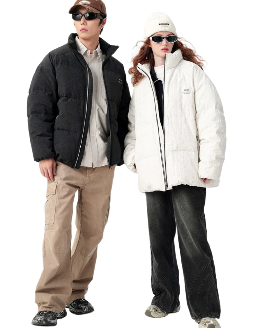 Full-body shot of models standing side-by-side in coordinating puffer jackets - black for man, white for woman, with matching accessories