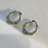 Silver twisted hoop earrings with alternating crystal and polished sections on white background, casting soft shadows